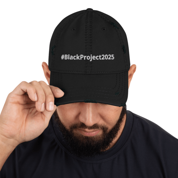 A man with a beard wearing a black cap embroidered with #BlackProject2025 in white text is tilting the brim of the hat down, partly covering his eyes. The background is transparent.