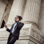 focused african american male employee speaking on smartphone using tws earphones in downtown